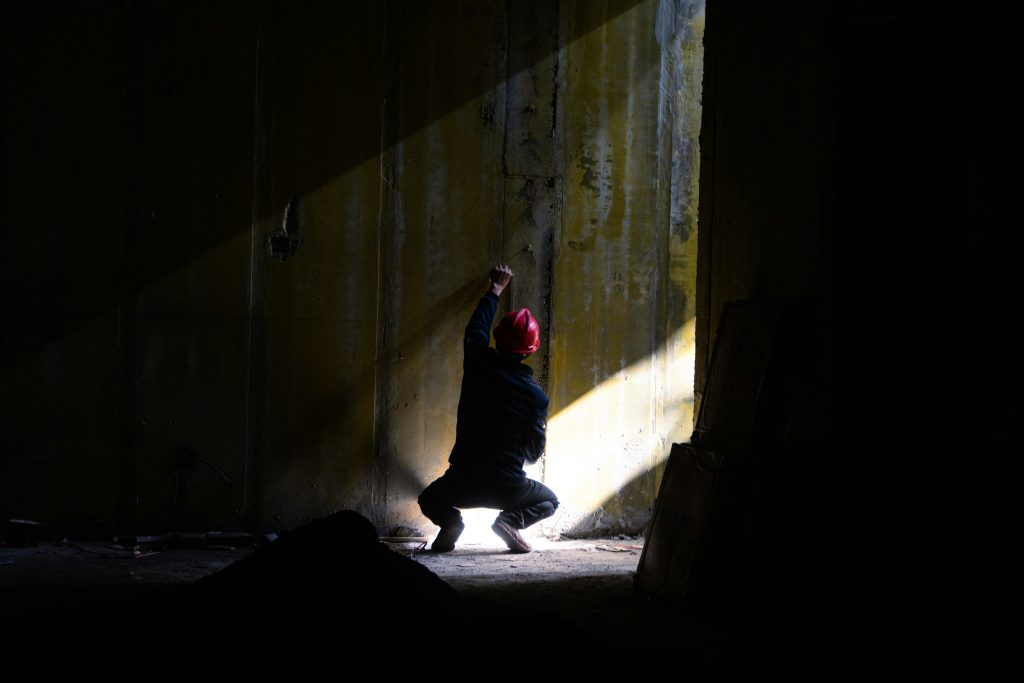 A person kneeling in a dark tunnel with only one sliver of light